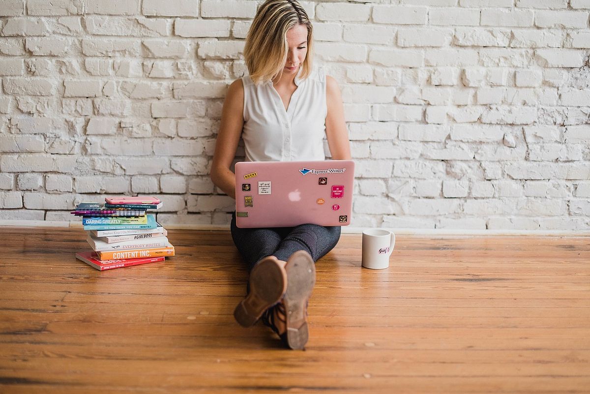 uma mulher com um laptop sentada no chão digitando